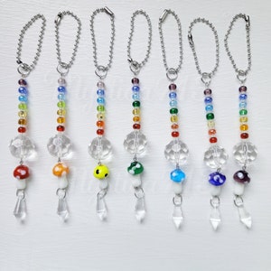 May include: Seven rainbow-colored beaded keychains with crystal charms shaped like mushrooms. Each keychain has a different colored mushroom with white spots.