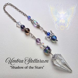 Könnte beinhalten: Ein dekorativer Sonnenfänger mit einem klaren Kristallpunkt, schillernden Perlen und einer silbernen Kette. Der Sonnenfänger hat ein himmlisches Thema mit dem Text "Umbra Stellarum" und "Shadow of the Stars".
