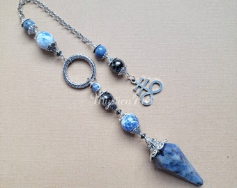 Puede incluir: Una cadena de plata con un colgante de piedra azul y blanca, un anillo de plata y un amuleto de plata con el símbolo del signo del infinito. El colgante es un cristal puntiagudo con una tapa de plata.