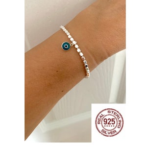 May include: A silver bracelet with a blue evil eye charm. The bracelet is made of small square beads and has a "REAL STERLING 925 SILVER" stamp.