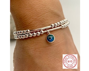 May include: Two silver bracelets with beaded strands and a dangling charm. The charm is a blue and green evil eye design. The bracelets are made of sterling silver.