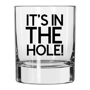 May include: A clear glass tumbler with the text "IT'S IN THE HOLE!" printed in black.