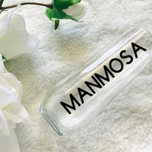 May include: A clear glass champagne flute with the word "MIMOSA" printed in black on the side.