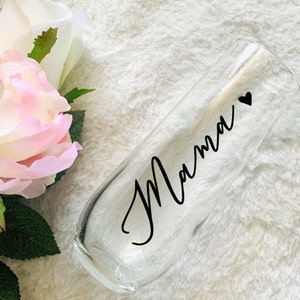 May include: A clear glass champagne flute with the word "Mamma" and a small heart written on it in black.