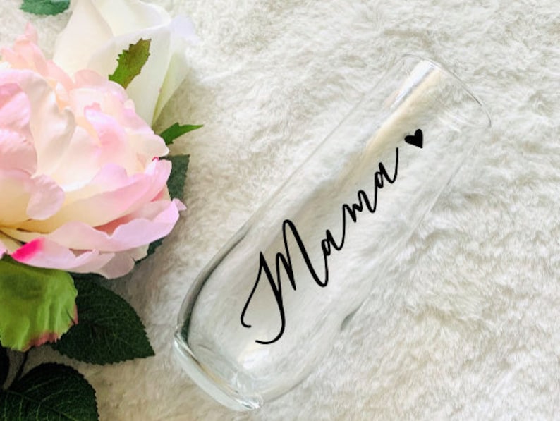 May include: A clear glass champagne flute with the word "Mamma" and a small heart written on it in black.