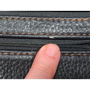 May include: Close-up of black leather with brown stitching and a zipper. The leather has a textured surface.