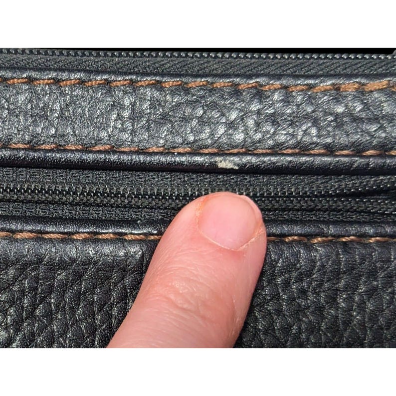 May include: Close-up of black leather with brown stitching and a zipper. The leather has a textured surface.