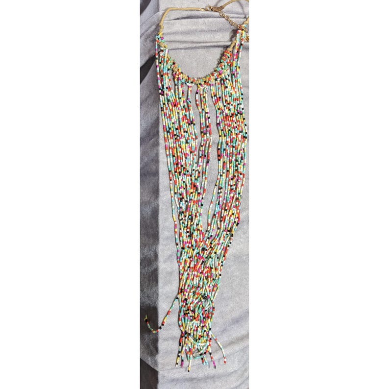 May include: A long, multi-strand necklace with small, colorful beads. The beads are in various colors, including red, yellow, black, and white. The necklace has a gold-colored chain and clasp.