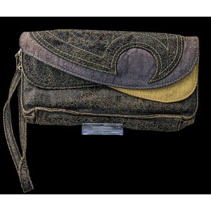 May include: A distressed clutch purse in black, grey, and olive green. The purse has a flap with a decorative stitched design and a wrist strap. The leather-like material has a cracked texture.