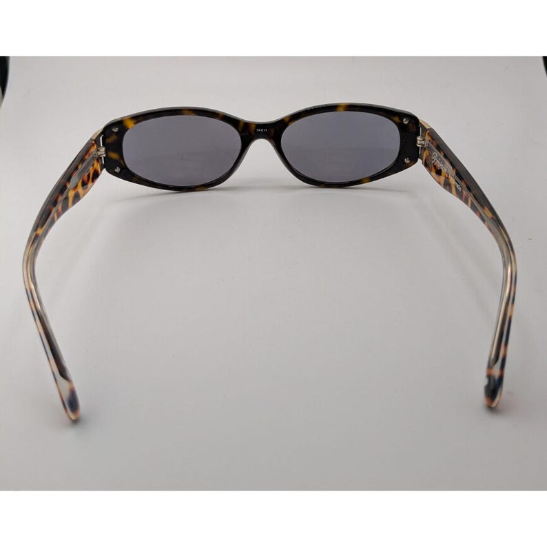 May include: Oval sunglasses featuring a brown and black tortoiseshell pattern frame with dark gray lenses. The temples extend outward from the frame, displaying the same tortoiseshell pattern, and the bridge connects the two oval-shaped lenses.