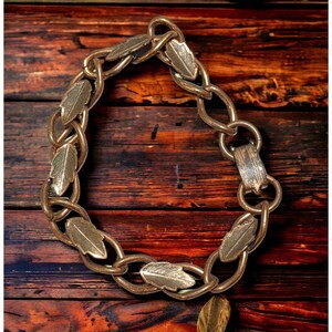 Op de afbeelding: Een gouden kettingarmband met bladeren als schakels. De armband is gemaakt van metaal en heeft een sluiting.