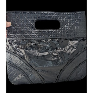 May include: Black clutch with a quilted top section and a glossy, textured bottom. The bag features a rectangular handle and two zippers on the sides. The overall design is sleek and modern.