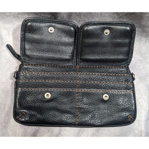 May include: Black leather wallet with multiple compartments and snap closures. The wallet has a brown stitching detail.
