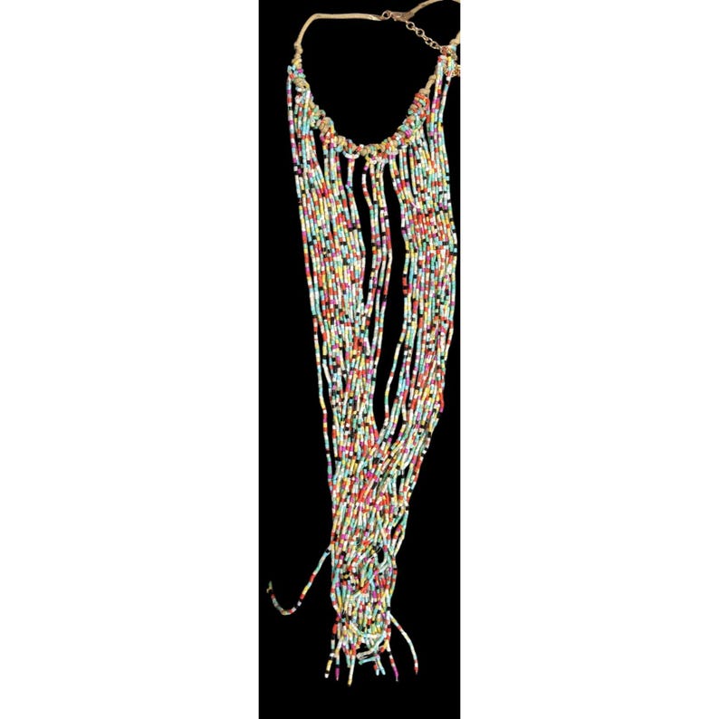 May include: A multi-strand necklace featuring a cascade of colorful beads in shades of red, yellow, blue, and green. The necklace has a gold-toned chain and a woven upper section. The beads are strung in a vertical, fringed design.