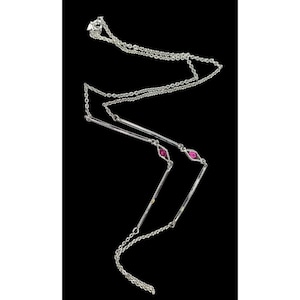 Op de afbeelding: Een zilveren ketting met een fijne ketting en drie verticale staven. Elke staaf is versierd met een roze edelsteen in een ruitvorm. De ketting wordt gepresenteerd tegen een zwarte achtergrond.
