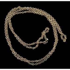 May include: A long, gold-toned chain necklace with multiple strands. The necklace is draped against a black background, showcasing its intricate link design. The chain appears to be made of metal and has a shiny finish.