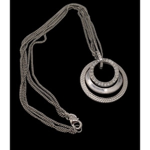 May include: Silver-toned necklace with a multi-strand chain and a pendant featuring three concentric circles. The middle circle is encrusted with small, clear crystals. The pendant hangs from a small loop at the top.