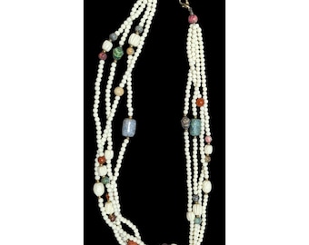 May include: Multi-strand necklace featuring off-white beads and decorative, colorful accent beads. The necklace has a variety of shapes and sizes of beads, including round, oblong, and rectangular. The accent beads are in shades of red, green, blue, and brown.