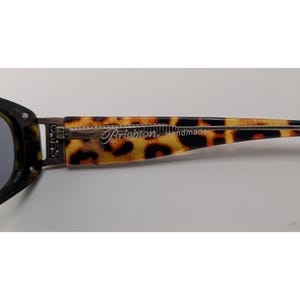 May include: Sunglasses with a brown and black tortoiseshell pattern on the temple arm. The temple features a silver-toned metal hinge with an ornate scroll design and the text Brighton Handmade printed in a script font along the side.