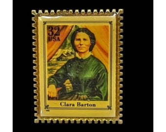 May include: A gold-toned rectangular pin featuring a vintage postage stamp design. The stamp depicts Clara Barton, with the text "32 USA" and "Clara Barton". The background shows a tent and landscape. The pin has a scalloped edge.