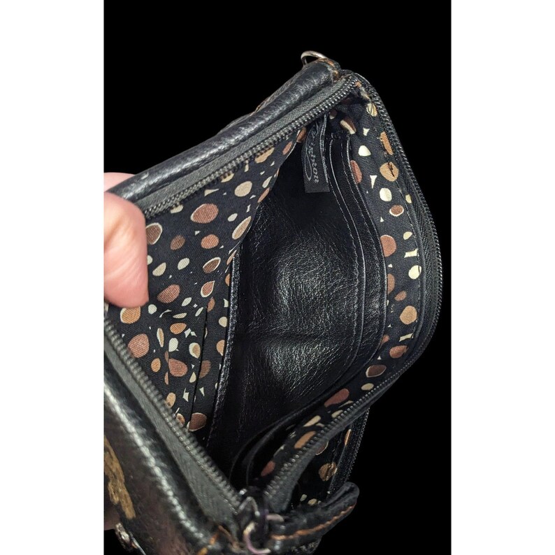 May include: Black leather purse with a zipper closure and a brown and white polka dot lining. The purse has a small pocket on the inside.