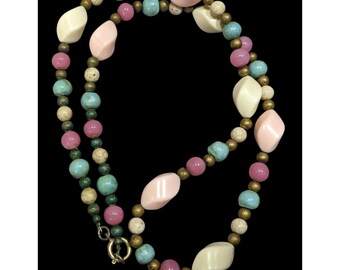 May include: A vintage necklace featuring a mix of beads in various shapes and colors. The necklace includes pink, blue, cream, and gold-toned beads. The necklace is displayed against a black background.
