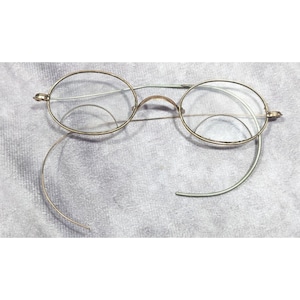 May include: A pair of antique gold-toned round eyeglasses with a wire frame and a thin metal nose bridge.