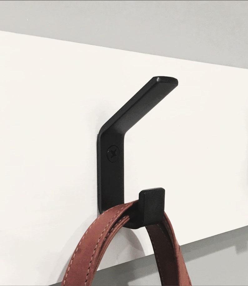 Black modern metal coat hook mounted to  wall board