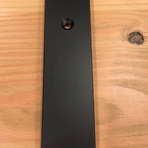 May include: A black metal bar with a rounded edge and a single hole in the center.