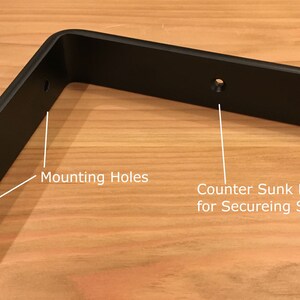 May include: Black metal shelf bracket with two mounting holes and a countersunk hole for securing shelf material.