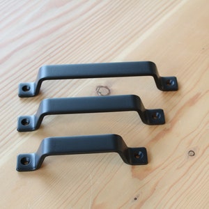 May include: Three black metal cabinet door pulls of different sizes. The pulls have a simple, rectangular design with rounded edges.