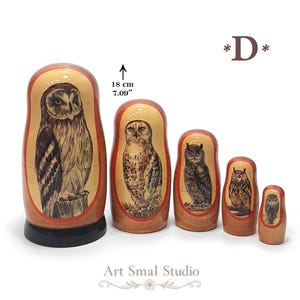 Five Russian nesting dolls featuring different hand-painted owls, with the largest showing a long-eared owl perched on a branch, followed by a pale owl, a dark horned owl, and two smaller owl figures. The 18 cm set is displayed from largest to smallest on a clean white background, with natural wood tones and red decorative borders. Model D