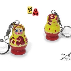 May include: A yellow and red wooden nesting doll keychain with a painted face and floral design. The keychain is attached to a silver metal ring.