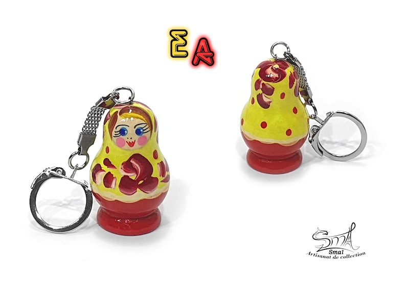 May include: A yellow and red wooden nesting doll keychain with a painted face and floral design. The keychain is attached to a silver metal ring.