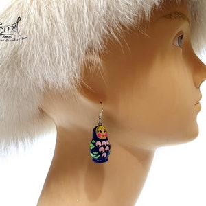 May include: A single Matryoshka doll earring. The earring is dark blue with a pink and green floral design. The doll has a yellow head and a pink face. The earring is hanging from a silver hook.