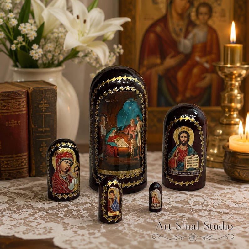 May include: A set of four dark brown nesting dolls featuring religious iconography. The largest doll depicts the Nativity scene, another shows Christ, and the smaller ones display figures of the Virgin Mary and a saint, all with gold-painted trim.