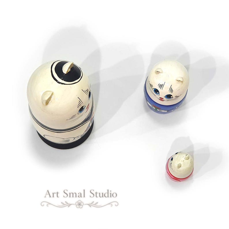 Viewed from above, three hand-painted cat sailor matryoshka dolls are arranged separately on a clean white background, showing the tops, cat ears and painted details of each wooden nesting doll