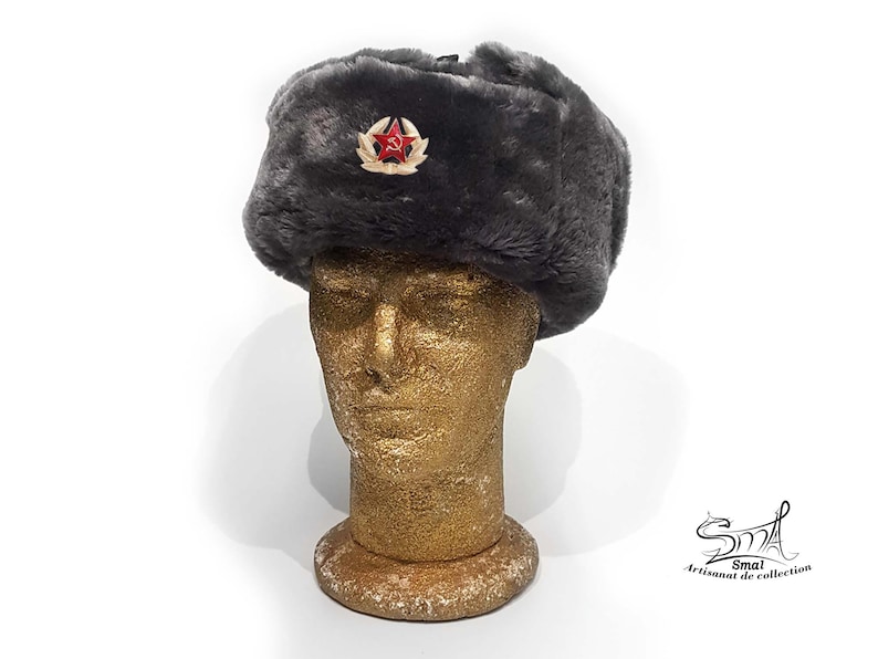 Op de afbeelding: Een grijze imitatiebont ushanka-muts met een rode ster en een hamer-en-sikkel-embleem.