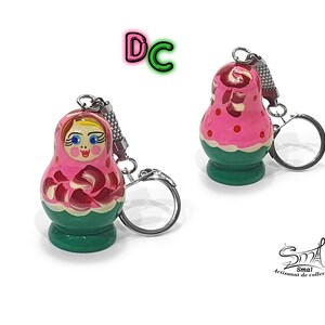 May include: A pink and green wooden nesting doll keychain with a painted face and floral design. The keychain has a silver metal ring.