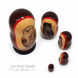 Top view of a Russian nesting doll set with five hand-painted owls, showing the dolls arranged separately from largest to smallest. The largest features a brown owl with a rounded head and no visible ear tufts, while the smaller pieces display different owl designs, including a dark owl with prominent ear tufts. The dolls have dark brown backs, red borders, natural wood-colored panels and glossy varnished surfaces. Model E, photographed on a white background