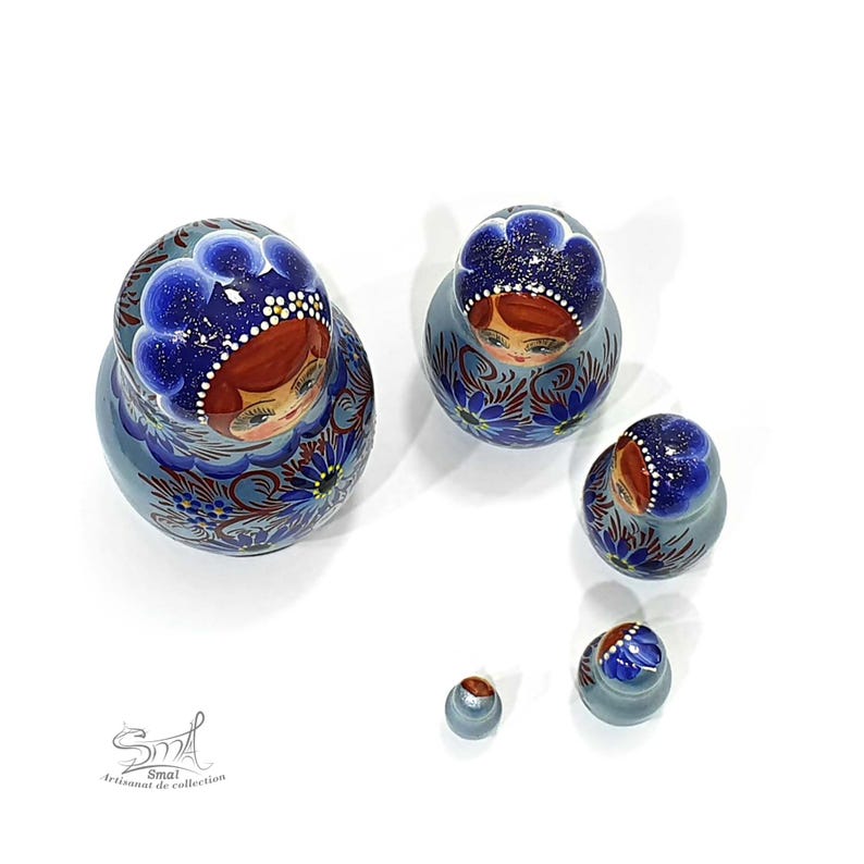 Vue plongeante sur les poupées gigognes russes bleu nacré de la collection Zoia. Cette perspective met en valeur la peinture du foulard, les détails réalisés à la main et la forme traditionnelle de chaque matriochka en bois.
