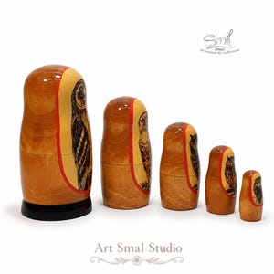 Right-side view of a five-piece Russian nesting doll set decorated with hand-painted owls. The dolls are shown from largest to smallest, revealing the natural wood backs, red painted borders and narrow owl illustrations along the side panels. The largest piece stands on a black base, and all five have a glossy varnished finish against a clean white background