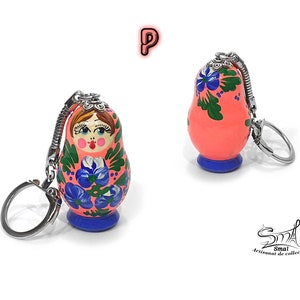 May include: Two Russian nesting doll keychains. The dolls are painted with a coral background, blue floral designs, and a blue base. Each keychain has a silver-colored metal ring and chain. The dolls have a traditional painted face.