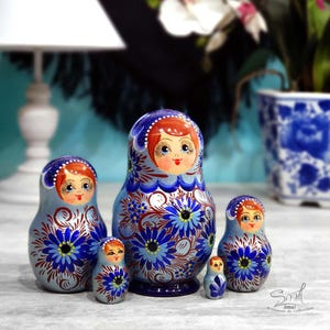 Ensemble de matriochkas russes bleu nacré présenté dans un intérieur contemporain. Les cinq poupées en bois sont disposées côte à côte afin de mettre en valeur leur taille, leur peinture artisanale et leurs délicats motifs floraux.