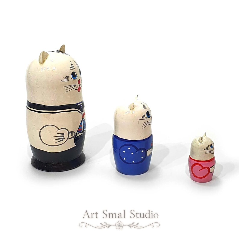 A side view of three hand-painted Russian cat sailor matryoshka dolls arranged separately on a clean white background, highlighting the nautical details and profiles of each wooden nesting figure