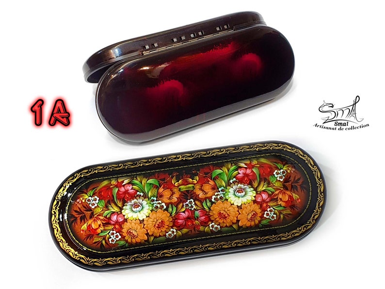 Puede incluir: Dos estuches para gafas de forma ovalada. El estuche superior es negro con un interior rojo. El estuche inferior es negro con un borde dorado y un dise&ntilde;o floral pintado en la tapa. El dise&ntilde;o presenta flores rojas, naranjas, amarillas y blancas sobre un fondo marr&oacute;n.