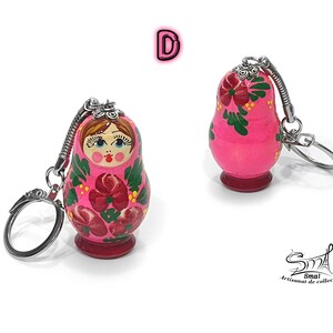 May include: Two pink Matryoshka doll keychains. The wooden dolls feature floral designs in red and green, with a painted face. Each keychain has a silver-colored metal ring and a spring-loaded connector.