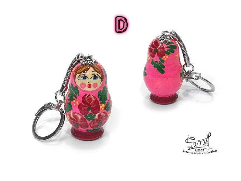 May include: Two pink Matryoshka doll keychains. The wooden dolls feature floral designs in red and green, with a painted face. Each keychain has a silver-colored metal ring and a spring-loaded connector.
