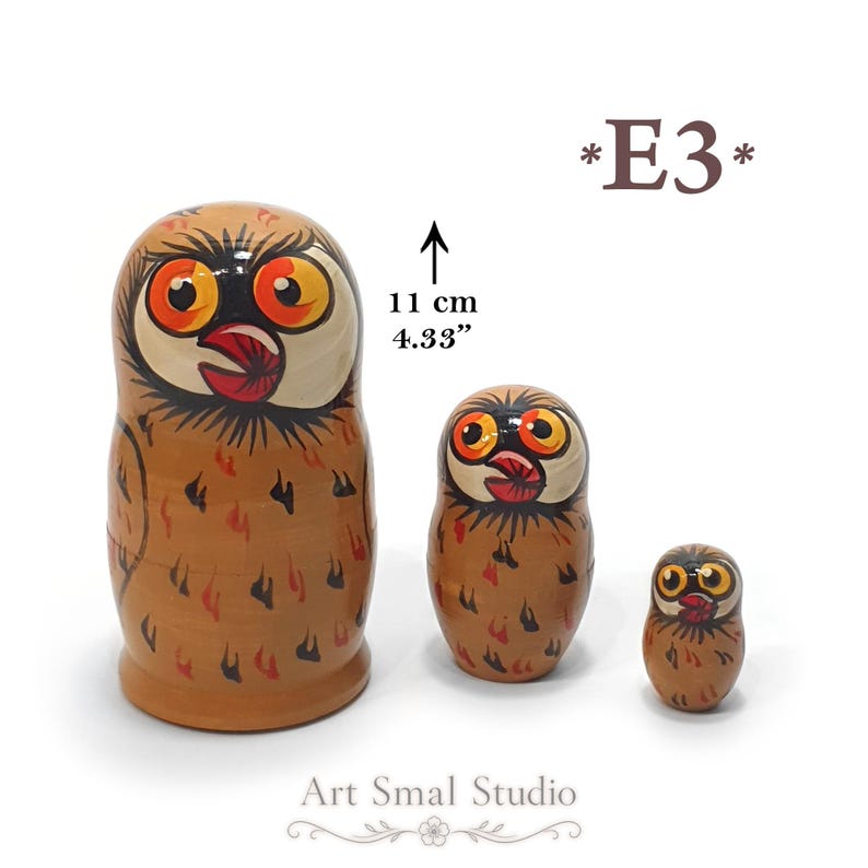 May include: Three wooden nesting dolls painted as brown owls with large orange eyes and black details. The largest doll is 11 cm or 4.33 inches tall. The text *E3* appears in the top right, and Art Smal Studio is printed at the bottom.