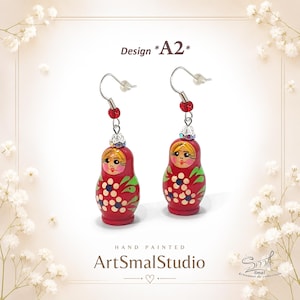 Hand-painted matryoshka doll earrings – Design A2. Charming red Russian nesting doll earrings featuring delicate floral patterns, rosy cheeks, blonde hair details, and tiny blue and white flowers. Lightweight folk-art inspired dangle earrings with silver-tone hooks and sparkling bead accents. Whimsical handmade jewelry by ArtSmalStudio.